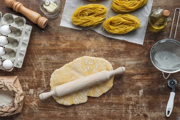 Top view of uncooked dough with rolling pin on wooden table — Stock Photo