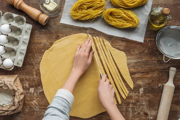 Vue du dessus de la pâte à découper les mains féminines pour pâtes sur une table en bois — Photo de stock