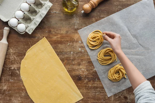 Vue du dessus des mains féminines mettant des pâtes crues sur papier à la table en bois — Photo de stock