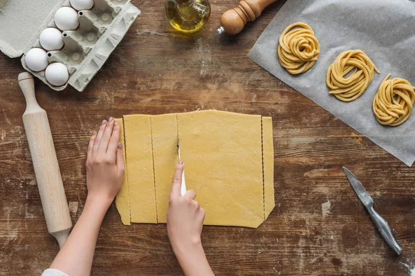 Top view of female hands cutting dough for pasta on wooden table — Stock Photo