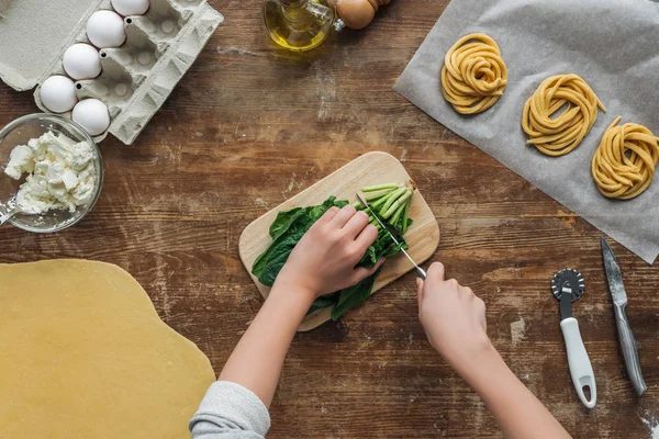 Vue de dessus des mains féminines coupant des épinards sur la table en bois — Photo de stock