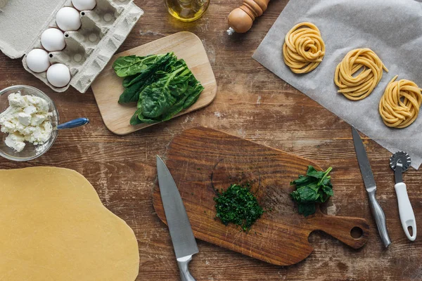 Vista dall'alto degli spinaci tagliati sul tagliere di legno e sugli ingredienti della pasta — Foto stock