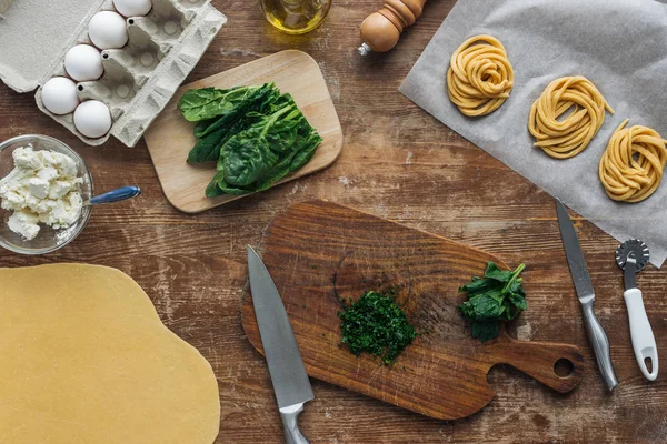 Vista superior de espinacas cortadas sobre tabla de cortar de madera e ingredientes de pasta - foto de stock