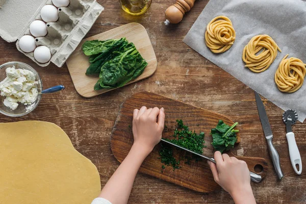 Top view of female hands cutting spinach on wooden chopping board — Stock Photo