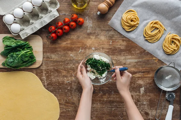 Vue du dessus des mains féminines mélangeant épinards et fromage crémeux dans un bol sur une table en bois — Photo de stock