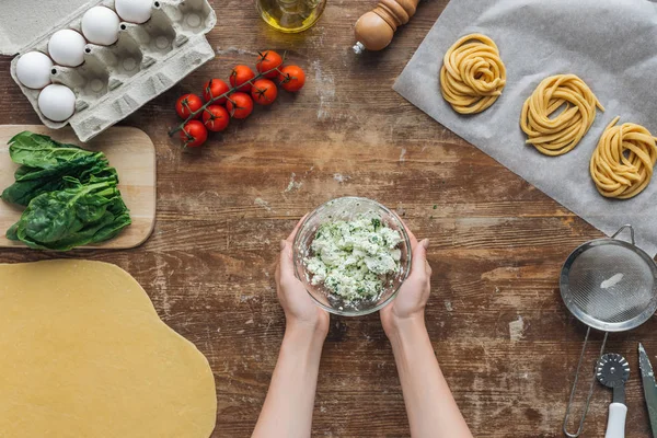 Vue du dessus des mains féminines et bol aux épinards et fromage crémeux sur table en bois — Photo de stock