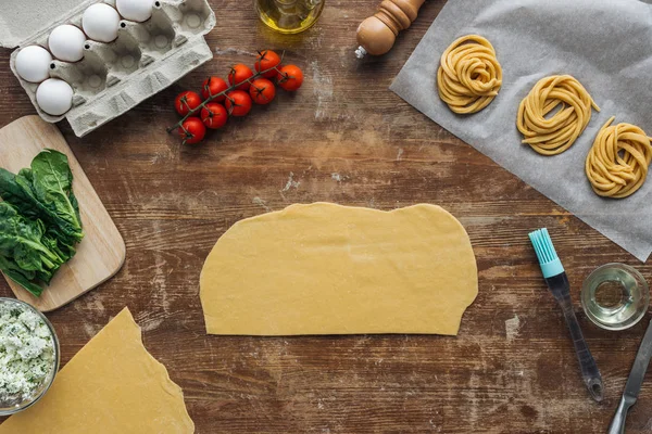 Draufsicht auf geschnittene rohe Teigstücke und Nudelzutaten auf Holztisch — Stockfoto