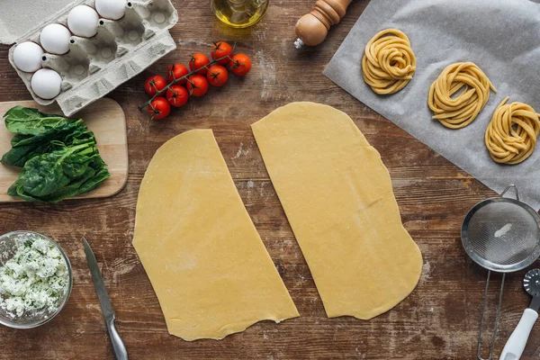 Draufsicht auf geschnittene rohe Teigstücke und Nudelzutaten auf Holztisch — Stockfoto