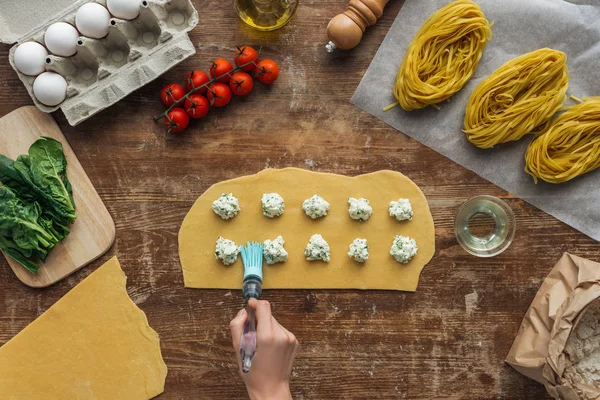 Vista dall'alto di mani femminili impasto oliante per ravioli con pennello imbastitura a tavola di legno — Foto stock