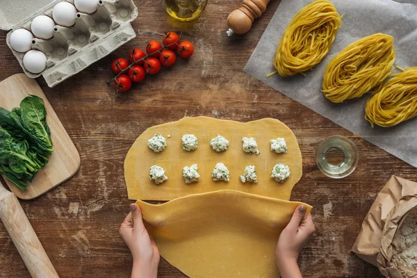 Vue de dessus des mains féminines couvrant la pâte avec remplissage pour raviolis à la table en bois — Photo de stock