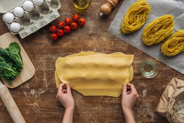 Vue de dessus des mains féminines couvrant la pâte avec remplissage pour raviolis à la table en bois — Photo de stock