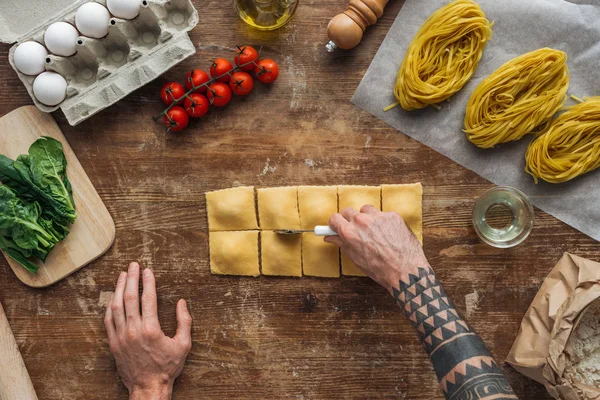 Vista dall'alto delle mani maschili ritagliare i ravioli con la ruota della pasticceria al tavolo di legno — Foto stock