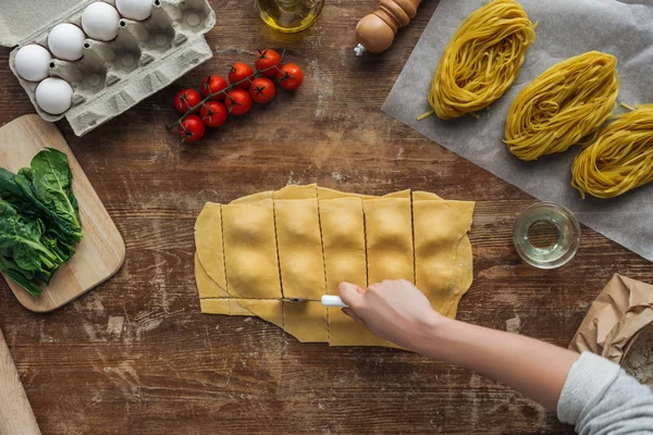 Vista superior de mãos femininas cortando ravioli na mesa de madeira — Fotografia de Stock