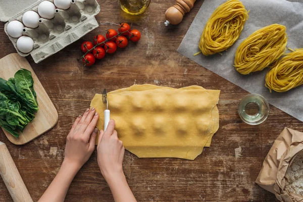Vue de dessus des mains féminines découpant des raviolis avec roue à pâtisserie à la table en bois — Photo de stock