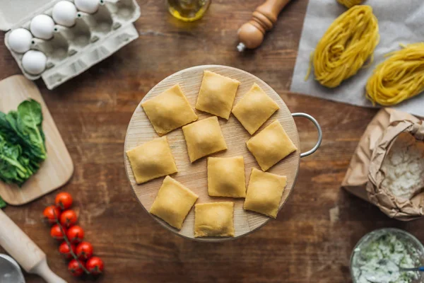 Vue du dessus des raviolis crus sur planche à découper à table en bois — Photo de stock