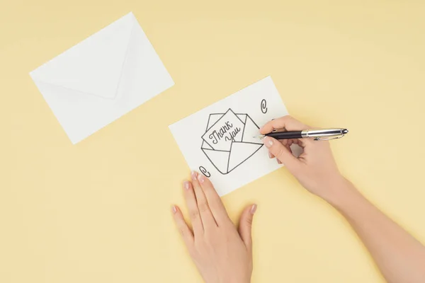 Persona recortada escribiendo tarjeta blanca con letras de agradecimiento sobresaliendo de sobre dibujado a mano aislado sobre fondo amarillo - foto de stock