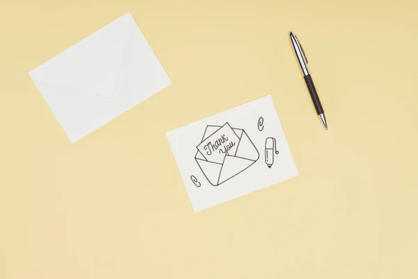 Tarjeta blanca con letras de agradecimiento que sobresalen del sobre dibujado a mano y pluma aislada sobre fondo amarillo — Stock Photo