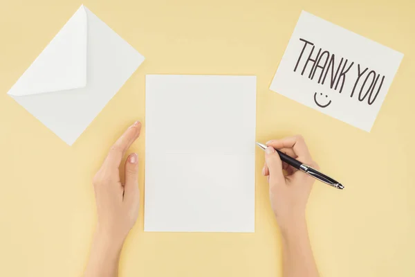 Cropped person holding pen, blank sheet, postcard with thank you lettering and smartpone isolated on yellow background — Stock Photo