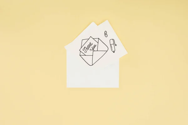 Tarjeta blanca con letras de agradecimiento que sobresalen de un sobre dibujado a mano aislado sobre fondo amarillo - foto de stock