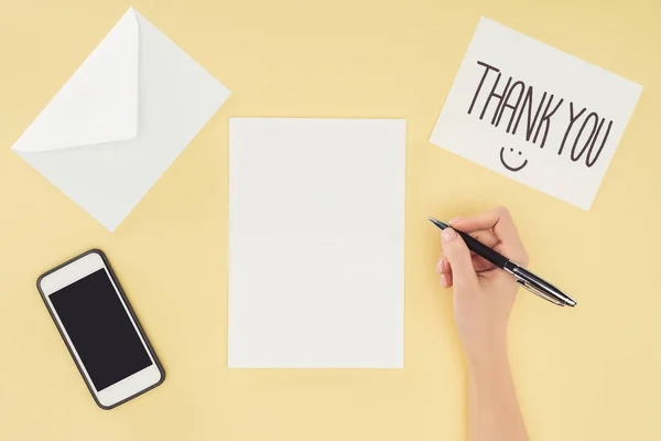 Cropped person holding pen, white postcard with thank you lettering and smartphone isolated on yellow background — Stock Photo