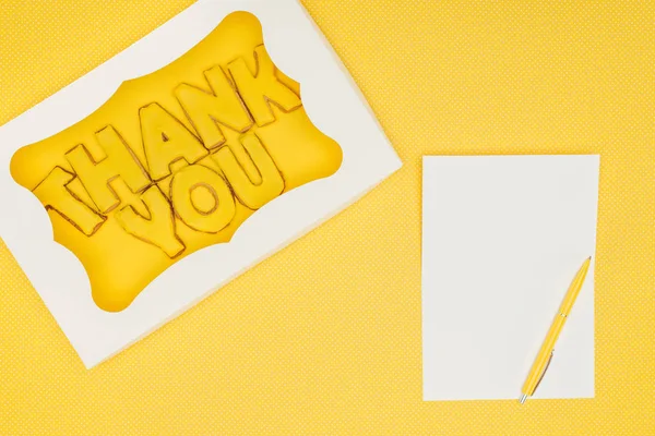 Square-shaped cake in box with thank you lettering and notebook isolated on yellow background — Stock Photo