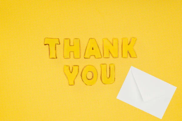 Thank you lettering in cookies with blank white envelope isolated on yellow background — Stock Photo