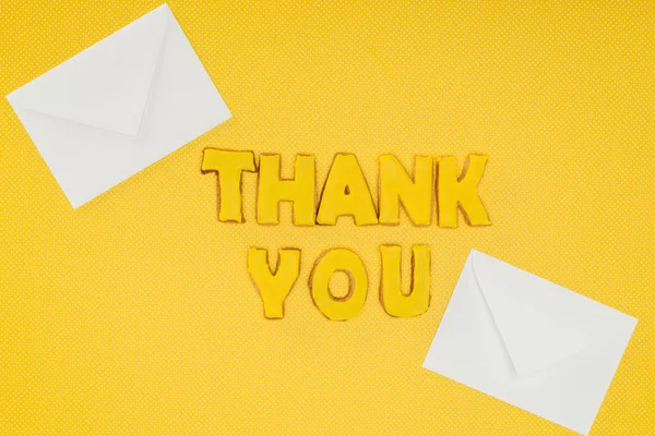 Thank you lettering in cookies with white envelopes isolated on yellow background — Stock Photo