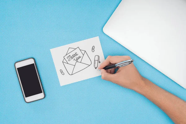 Corte vista do desenho da mão obrigado lettering saindo do envelope no cartão branco com smartphone isolado no fundo azul — Fotografia de Stock