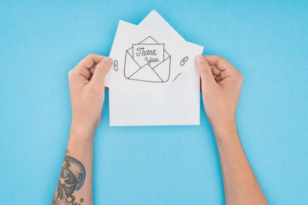 Abgeschnittene Person hält Papier mit Dankeschön-Schriftzug, der isoliert auf blauem Hintergrund aus dem Umschlag ragt — Stockfoto