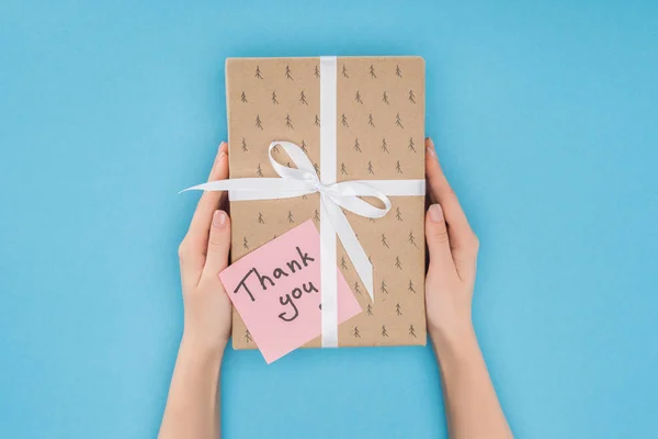 Persona recortada sosteniendo caja de regalo con nota adhesiva con letras de agradecimiento aislado sobre fondo azul - foto de stock