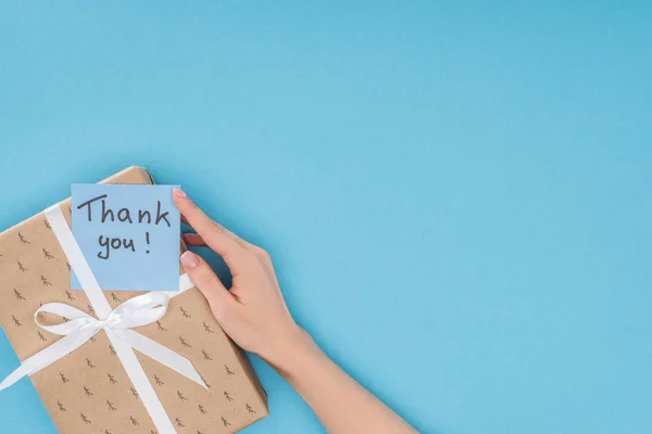 Vista ritagliata della mano e nota appiccicosa con scritte di ringraziamento sulla scatola regalo isolata su sfondo blu — Foto stock