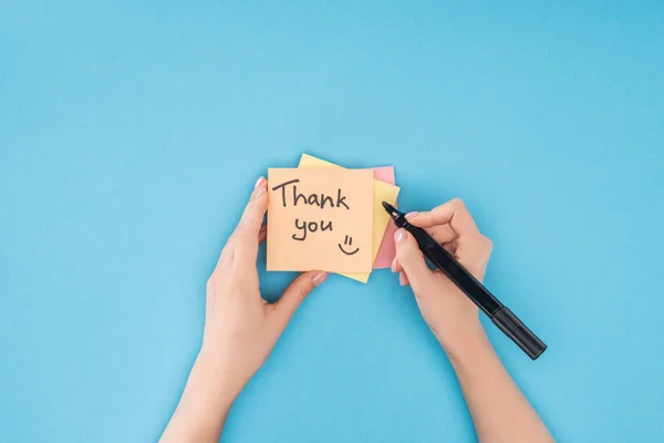 Abgeschnittene Person mit Stift über bunten Haftnotizen mit Dankeschön-Schriftzug auf blauem Hintergrund — Stockfoto