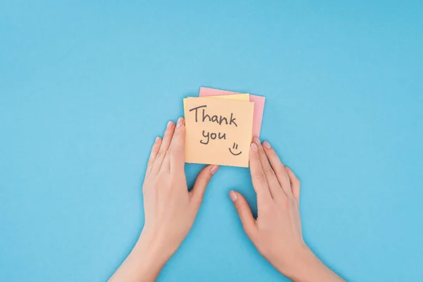 Pessoa cortada segurando notas pegajosas coloridas com letras de agradecimento isolado no fundo azul — Fotografia de Stock