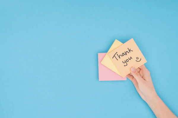 Pessoa cortada segurando notas pegajosas coloridas com letras de agradecimento isolado no fundo azul — Fotografia de Stock