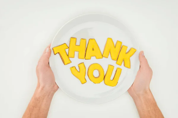 Cropped view of male hands holding white plate with thank you lettering made of cookies isolated on white background — Stock Photo