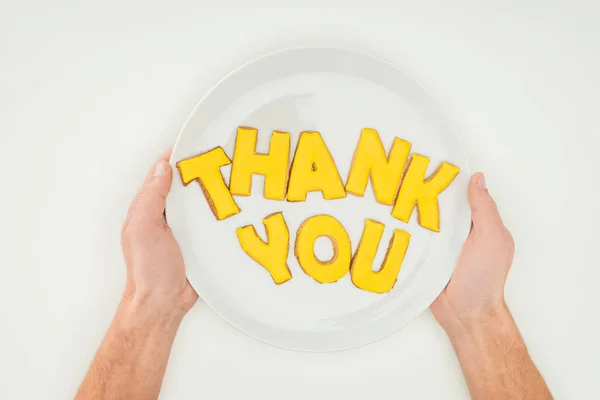 Vista recortada de manos masculinas sosteniendo placa blanca con letras de agradecimiento hechas de galletas aisladas sobre fondo blanco - foto de stock