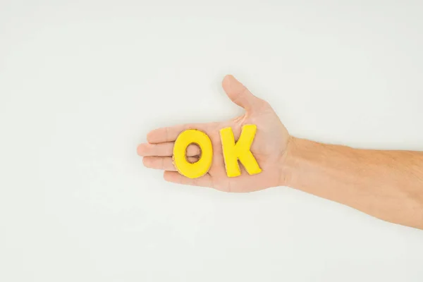 Vista recortada de la persona sosteniendo la palabra ok en galletas amarillas aisladas sobre fondo blanco - foto de stock