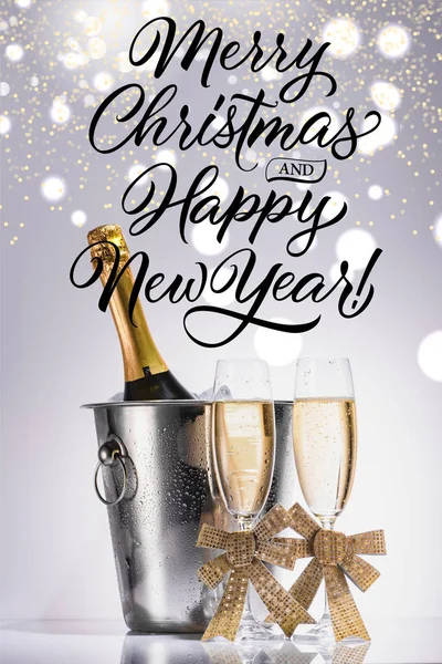 Bottle of champagne in bucket and glasses of champagne on grey backdrop with 