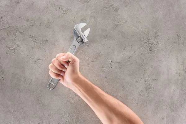 Tiro recortado del hombre que sostiene la llave de la tubería en la mesa de hormigón — Stock Photo