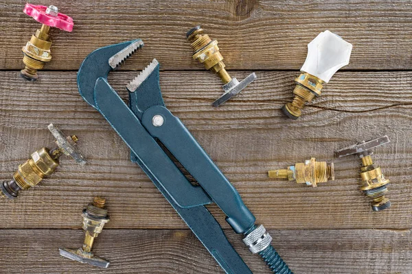 Top view of plumber wrench and different plumbing valves on rustic wooden tabletop — Stock Photo