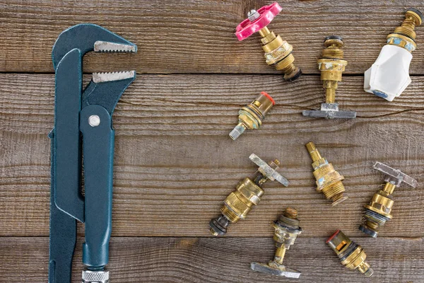 Draufsicht auf Klempnerschlüssel und verschiedene Sanitärventile auf rustikaler Holztischplatte — Stockfoto