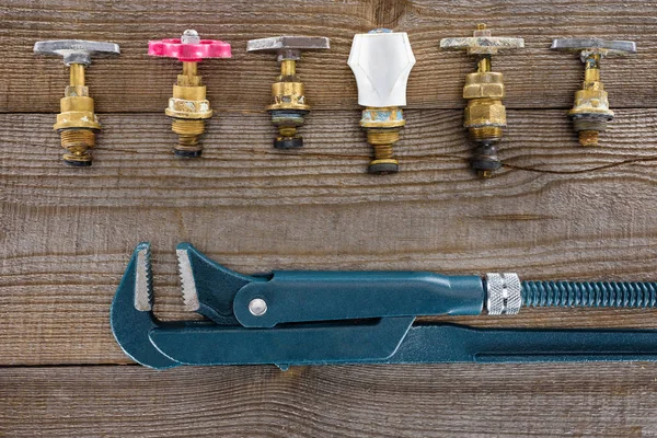 Верхний вид трубного ключа и различных водопроводных клапанов на деревенской деревянной столешнице — стоковое фото