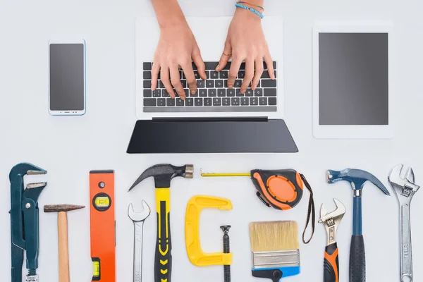 Tiro cortado de mulher usando laptop com várias ferramentas deitado no branco — Fotografia de Stock