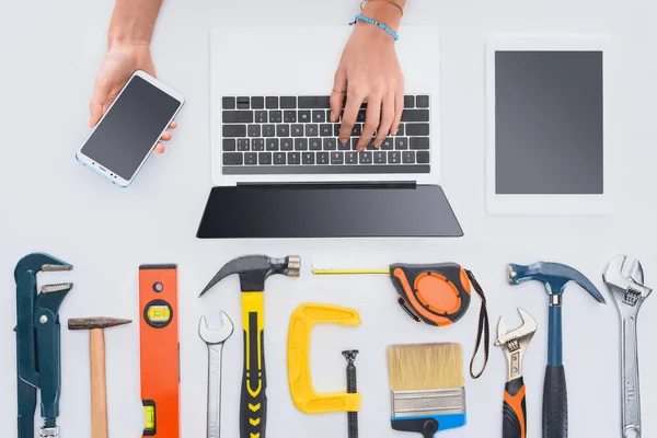 Cropped shot of woman using devices with various tools lying on white — Stock Photo