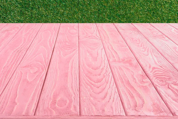 Surface of pink wooden planks on green grass background — Stock Photo