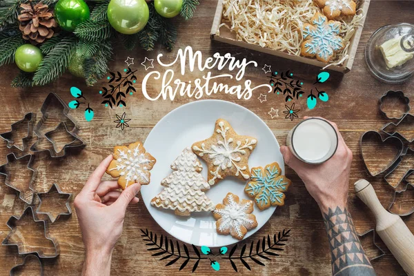 Cropped shot of man holding homemade christmas cookie and glass of milk on wooden surface with 