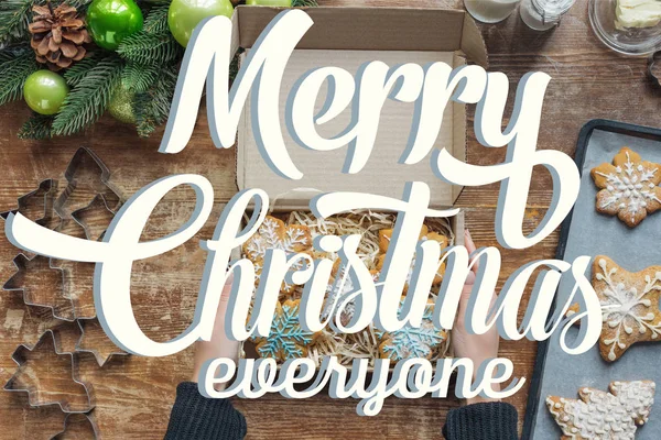 Cropped shot of woman holding box with  homemade christmas cookies on wooden tabletop with decorative christmas wreath with 