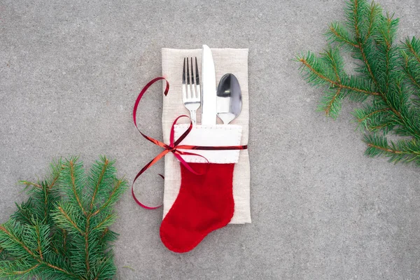 Vista dall'alto della forchetta, cucchiaio con coltello in calza di Babbo Natale avvolto da nastro rosso sul tavolo con rami sempreverdi — Foto stock