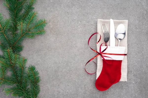 Vista sopraelevata di forchetta, cucchiaio con coltello in calza di Babbo Natale avvolto da nastro rosso su tavolo con rami sempreverdi — Foto stock