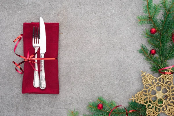Elevated view of fork and knife wrapped by red ribbon on table with evergreen branch decorated by christmas balls and golden christmas star — Stock Photo